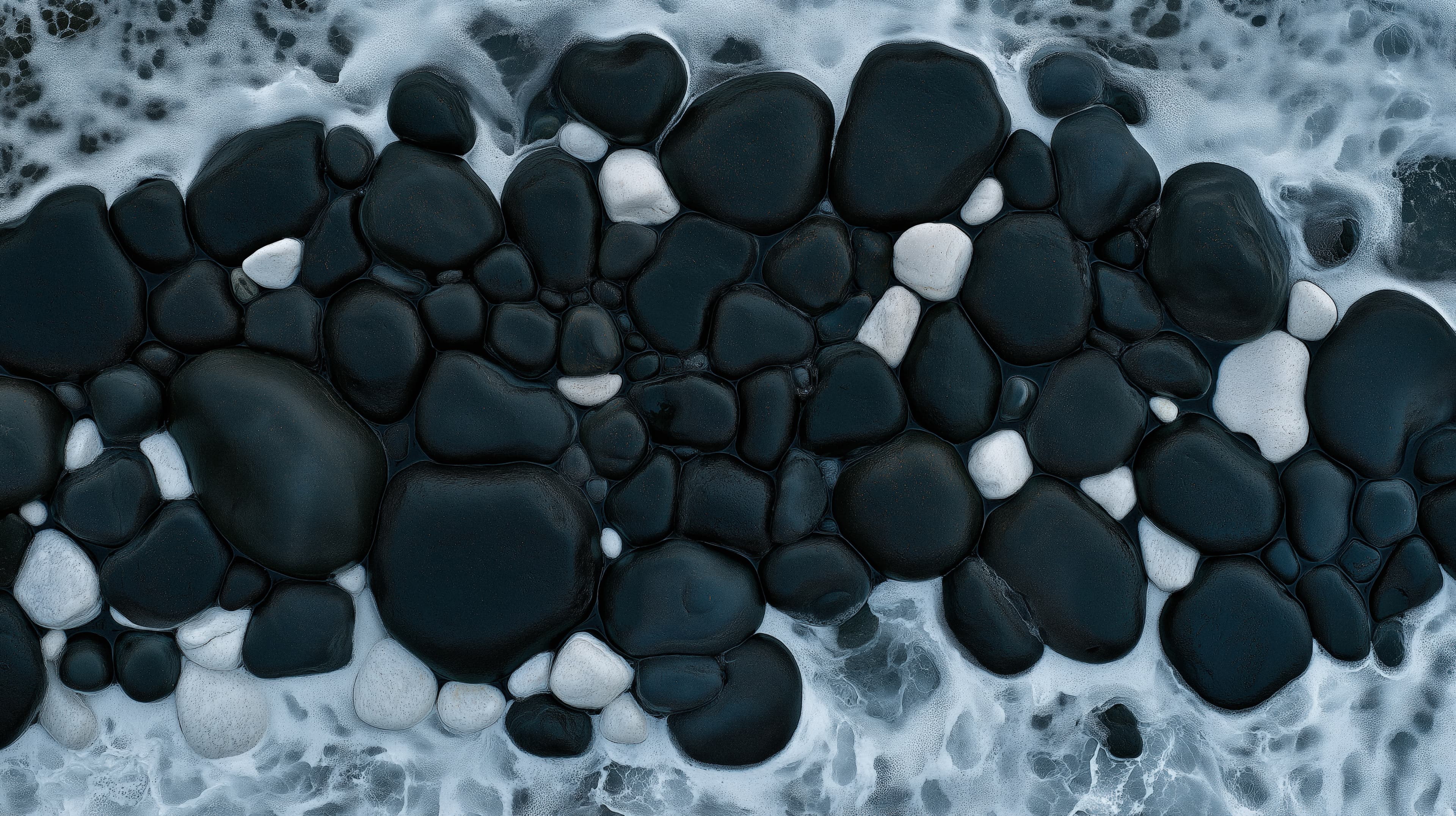 Close-up of a group of black and white pebbles arranged in a random pattern. the pebble stones are of different sizes and shapes, with some being larger and some being smaller.